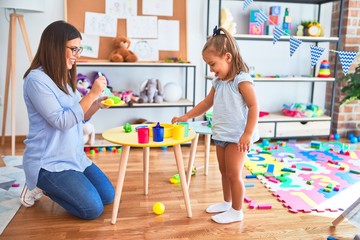 Caucasian girl kid playing and learning at playschool with female teacher. Mother and daughter...