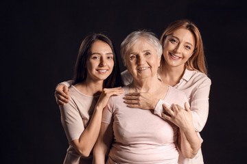 Portrait of mature woman with her adult daughter and mother on dark background