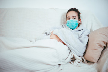 Pretty girl with mask sitting on a sofa, quarantining for viruses