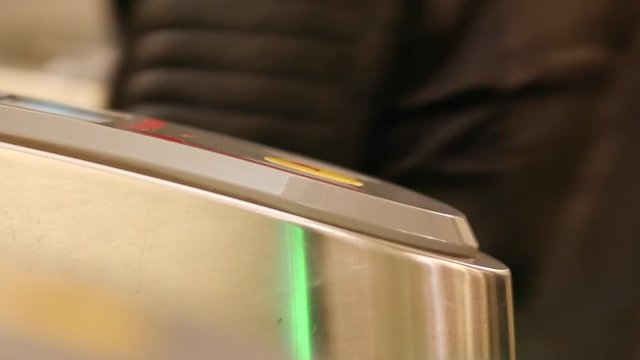 People go into the subway through an electronic barrier. Ring with NFC RFID. A hand in a black glove applies to a contactless reader at the gate of a subway turnstile. Green LED backlight.