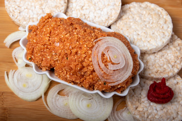 veganes mett, Brotaufstrich mit Zwieben umgeben von Reiswaffeln, Zwiebeln und Tomatenmark, in einer Schale auf einem Holzbrett, Textfreiraum