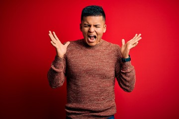 Young handsome latin man wearing casual sweater standing over red background celebrating mad and...