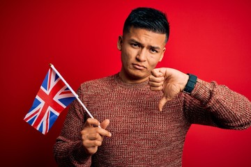 Young handsome latin patriotic man wearing united kingdom flag over red background with angry face,...