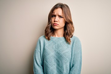 Young blonde girl wearing casual blue winter sweater over isolated background skeptic and nervous,...