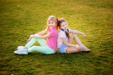 Happy cute girls sit on the grass by the children in the park