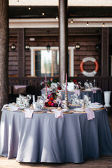 Wedding banquet. Served round festive table with a blue tablecloth decorated with a floral arrangement of red flowers and candles in the center of the table. Side view