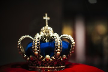 Closeup selective focus shot of a blue crown with pearls on it on a red pillow