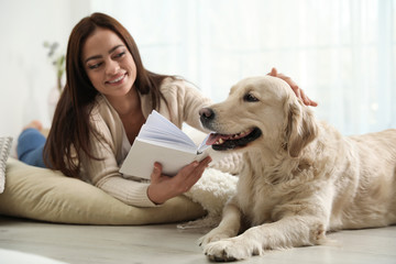 Young woman with book and her Golden Retriever at home. Adorable pet