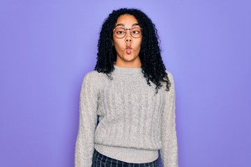 Young african american woman wearing casual sweater and glasses over purple background making fish face with lips, crazy and comical gesture. Funny expression.