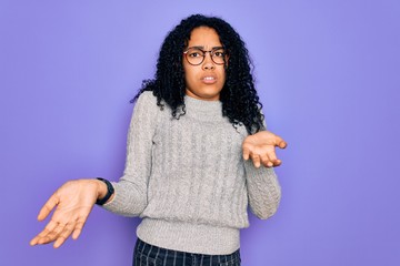 Young african american woman wearing casual sweater and glasses over purple background clueless and confused with open arms, no idea concept.