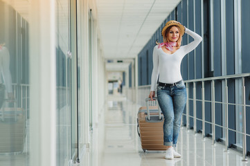 Casually dressed young stylish female traveller checking a departures board at the airport terminal hall in front of check in couters. Flight schedule display blured in the background. Focus on woman.