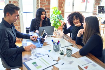 Fototapeta premium Group of business workers smiling happy and confident. Working together with smile on face using laptop and speaking at the office