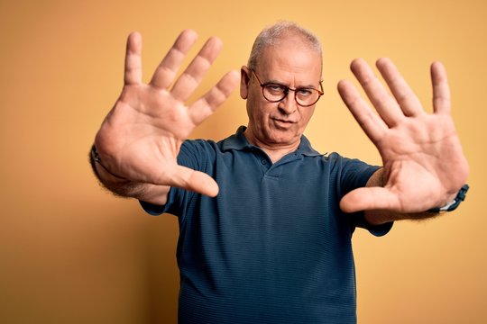 Middle age handsome hoary man wearing casual polo and glasses over yellow background doing frame using hands palms and fingers, camera perspective
