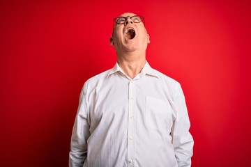 Middle age handsome hoary man wearing casual shirt and glasses over red background angry and mad screaming frustrated and furious, shouting with anger. Rage and aggressive concept.
