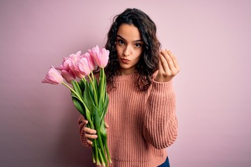 Young beautiful romantic woman with curly hair holding bouquet of pink tulips Doing Italian gesture with hand and fingers confident expression