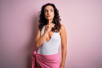 Beautiful woman with curly hair on vacation wearing white swimsuit over pink background Thinking...