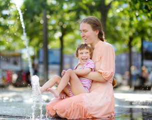 Portrait of beautiful disabled girl in the arms of his mother having fun in fountain of public park...