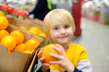 Fototapeta na wymiar Cute little boy in a food store or a supermarket choosing fresh organic oranges.