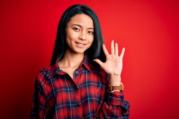 Young beautiful chinese woman wearing casual shirt over isolated red background showing and pointing up with fingers number five while smiling confident and happy.