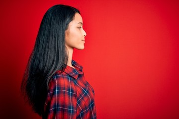 Young beautiful chinese woman wearing casual shirt over isolated red background looking to side, relax profile pose with natural face and confident smile.