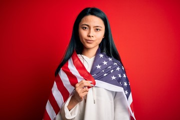 Young beautiful chinese woman wearing United States flag over isolated red background with a...