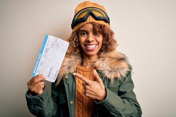 Young african american tourist woman wearing ski goggles holding plane boarding pass tickets very happy pointing with hand and finger