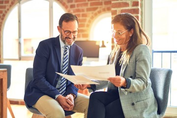 Two middle age business workers smiling happy and confident. Working together with smile on face reading documents at the office