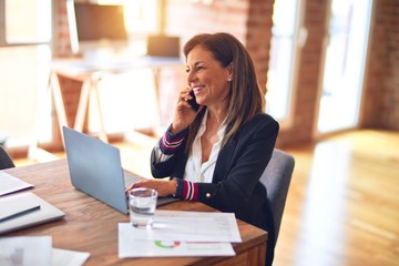 Middle age beautiful businesswoman smiling happy and confident. Sitting on chair working in a desk...