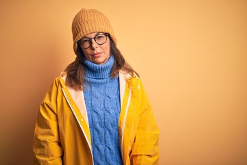 Middle age woman wearing yellow raincoat and winter hat over isolated background Relaxed with...