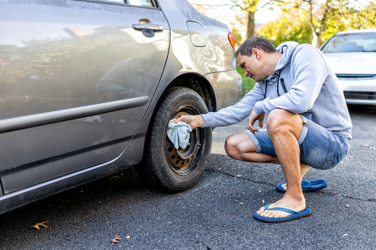 Person cleaning tire wheel with missing cap cover on parked car with man rubbing rusty hubcap with towel