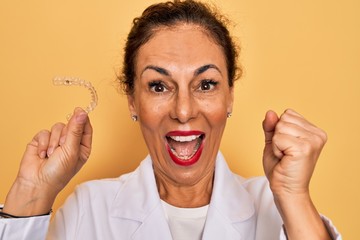 Middle age senior dentist woman holding clear aligner for teeth correction screaming proud and...