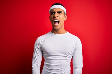 Young handsome african american sportsman wearing sportswear over red background angry and mad...
