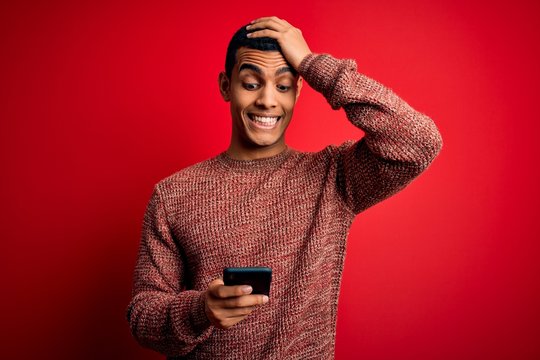 Handsome african american man having conversation using smartphone over red background stressed with hand on head, shocked with shame and surprise face, angry and frustrated. Fear and upset