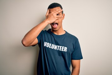 Young handsome african american man volunteering wearing t-shirt with volunteer message peeking in...