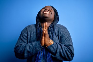 African american plus size woman with braids wearing casual sweater over blue background begging...