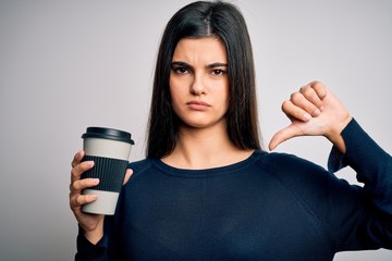 Young beautiful brunette woman drinking cup of coffee over isolated white background with angry...
