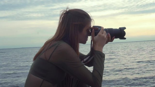 A girl photographer sits on a stone shore and takes pictures. Natural landscape