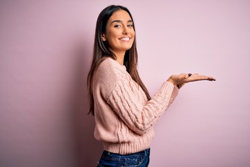 Young beautiful brunette woman wearing casual sweater over isolated pink background pointing aside...