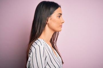 Young beautiful brunette woman wearing casual striped shirt over isolated pink background looking to side, relax profile pose with natural face with confident smile.