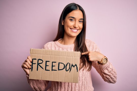 Young beautiful brunette activist woman protesting for freedom holding poster with surprise face pointing finger to himself