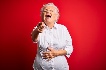 Senior beautiful woman wearing elegant shirt standing over isolated red background laughing at you, pointing finger to the camera with hand over body, shame expression