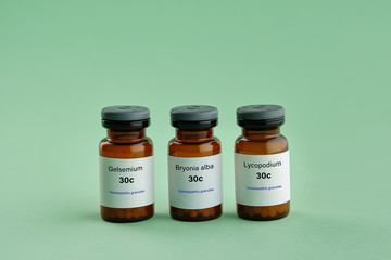 Bottles of homeopathic drugs - Gelsemium, Bryonia alba, Lycopodium - remedies recommended by homeopaths for treatment and prophylaxis of Coronavirus Covid-19 Infection. Green background.