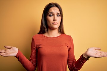 Obraz premium Young beautiful brunette woman wearing casual t-shirt standing over yellow background clueless and confused with open arms, no idea concept.