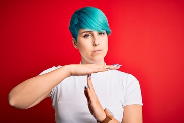 Young beautiful woman with blue fashion hair wearing casual t-shirt over red background Doing time...