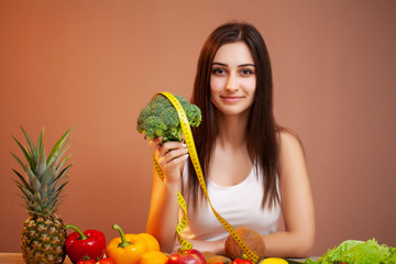 Fototapeta premium Cute woman at a table holding a broccoli on a background of fruit and vegetables