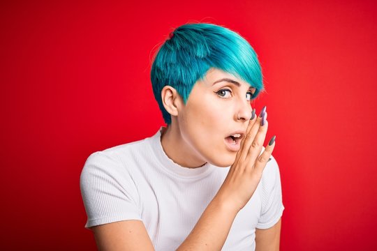 Young Beautiful Woman With Blue Fashion Hair Wearing Casual T-shirt Over Red Background Hand On Mouth Telling Secret Rumor, Whispering Malicious Talk Conversation