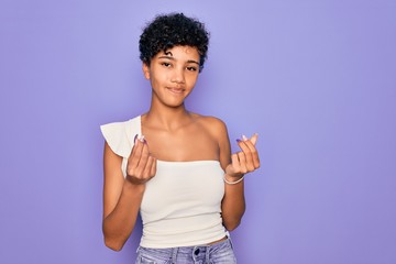 Fototapeta na wymiar Young beautiful african american afro woman wearing casual t-shirt over purple background doing money gesture with hands, asking for salary payment, millionaire business