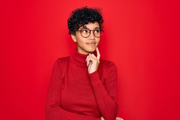 Fototapeta na wymiar Young beautiful african american afro woman wearing turtleneck sweater and glasses with hand on chin thinking about question, pensive expression. Smiling and thoughtful face. Doubt concept.