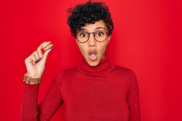 Young beautiful african american afro woman holding chocolate french dessert macaron scared in shock with a surprise face, afraid and excited with fear expression