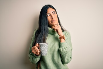 Young beautiful hispanic woman drinking a cup of hot coffee over isolated background serious face...